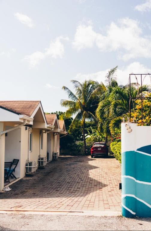 Oprit van het resort met bestrating, palmboom en geparkeerde auto
